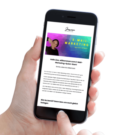 Mockup-EMQ (1) Eine Hand hält ein Smartphone, auf dem eine Willkommensnachricht für eine Kurzanleitung zum E-Mail-Marketing starten angezeigt wird. Auf dem Bildschirm sind Text und ein buntes Banner zu sehen, ein Finger ist am unteren Bildschirmrand positioniert.