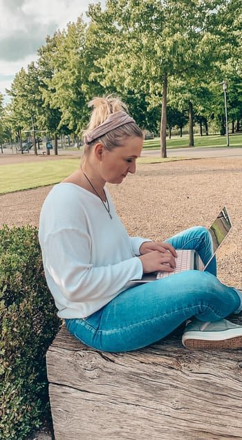 Tatjana sitzt mit ihrem Laptop im Grünen.